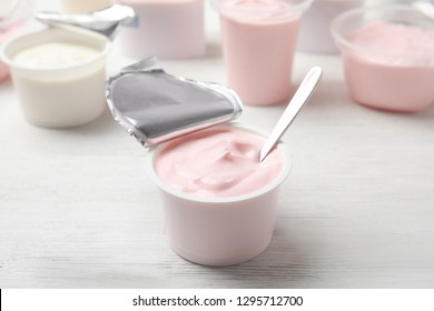 Plastic Cup With Fresh Yogurt And Spoon On White Wooden Table