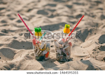 Plastic cups with straw and tropical decor and Garbage on the beach, trash, plastic, bottle, foam, rubbish, sigarette stub. Ecological creative concept, trash cocktail on the beach 
