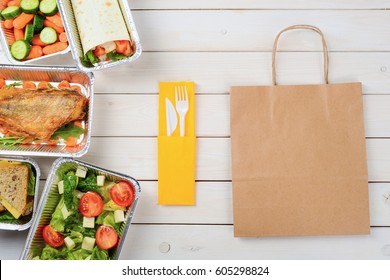 Plastic Cutlery And A Paper Bag On The Wooden Surface. Tomato And Feta Salad, Cheese Sandwiches, Fish With Arugula, A Vegetable Roll, A Sliced Cucumber And Baby Carrots. Dinner Food Delivery.