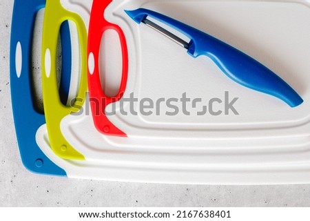Plastic cutting boards in different colors and sizes, and vegetable peeler close-up, flat lay
