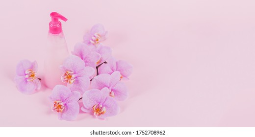 Plastic dispenser bottle with liquide cosmetic soap, intimate wash or shower gel, purple sponge and pink orchid flowers on light pink background. Spa and women's hygiene concept