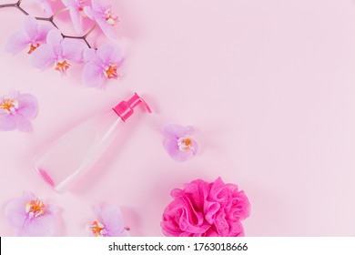 Plastic dispenser bottle with liquide cosmetic soap, intimate wash or shower gel, purple sponge and pink orchid flowers on light pink background. Spa and women's hygiene concept