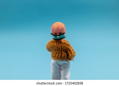 Plastic doll wearing a face mask against a blue background. Room for copy. 