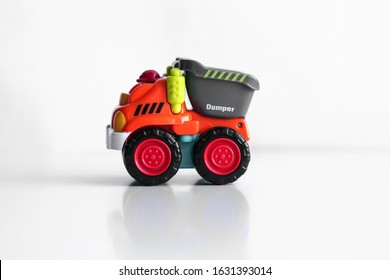 Plastic Dump Truck Toy Construction Vehicle Isolated On White Background With Reflection. Dumper Side View. Orange Vehicle With Red Wheels And Name Text. Operator In Red Hard Hat