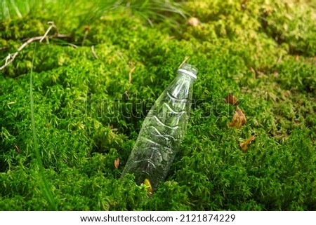A plastic empty transparent bottle sticks out of the moss in the forest. Pollution of the planet with non-decomposing garbage and waste of production and vital activity. Environmental protection.
