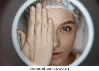 Plastic Facial Surgery Concept. Close Up Young Attractive Woman Lying And Looking Straight. She Cover Face Prt With Hand. Serious Client Look Through Light Hole.