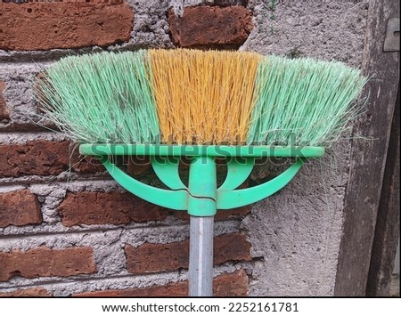 A plastic floor broom in an upside down position leaning against a brick wall.
