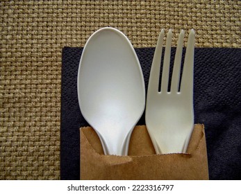 Plastic  Fork And Spoon On A Black Napkin Against A Background Of Coarse Fabric