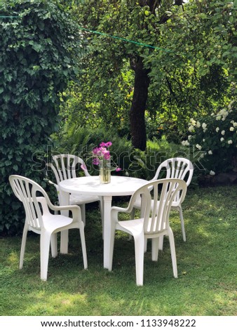 Plastic furniture set from nineties in super green garden environment. White chair and table and wild flowers in the glass. Vintage feeling