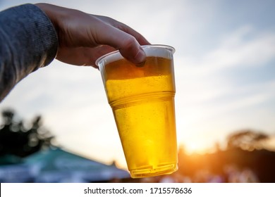 Plastic Glass Of Beer In Hand At Sunset.