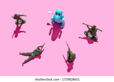 Plastic Green Army Men Surrounding A Tyrannosaurus Rex On A Pink Background