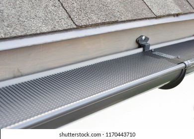 Plastic Guard Mesh Over New Dark Grey Plastic Rain Gutter On Asphalt Shingles Roof At Shallow Depth Of Field.
