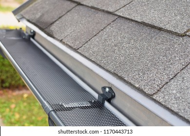 Plastic Guard Mesh Over New Dark Grey Plastic Rain Gutter On Asphalt Shingles Roof At Shallow Depth Of Field.
