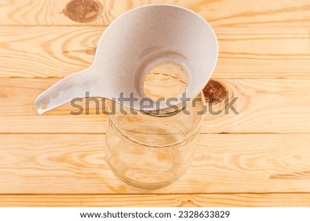 Plastic kitchen funnel for pouring liquids and powders on the empty glass jar with wide mouth on a rustic table, top view
