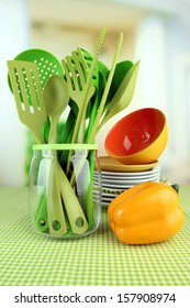 Plastic kitchen utensils in stand with clean dishes on tablecloth on bright background