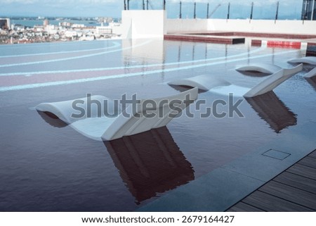 Plastic lounge deckchairs inside infinity swimming pool with city view. Holiday or vacation concept.