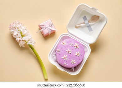 Plastic Lunch Box With Tasty Bento Cake, Gift And Flowers On Beige Background