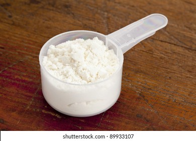 plastic measuring scoop of white powder (whey protein) against grunge wood background