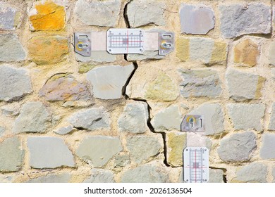 Plastic mechanical crack meter to measure movement across surface cracks and joints - concept with deep crack in a damaged old stone wall cause due to subsidence of foundations structural failures