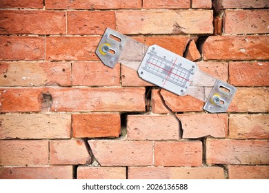 Plastic mechanical crack meter to measure movement across surface cracks and joints - concept with deep crack in a damaged old brick wall cause due to subsidence of foundations structural failures