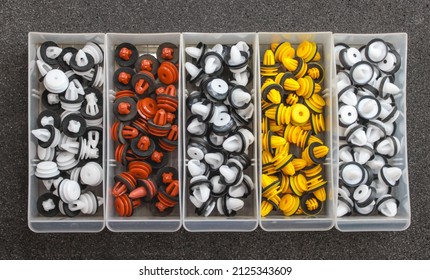 Plastic multi-colored clips for a car in a container box on a gray background. Car clips, plastic fasteners, colorful plastic clips close-up in a box. Car clips and fasteners close-up.