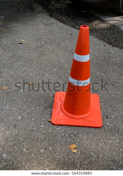 Plastic orange cone on\
the asphalt road