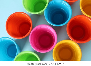 Plastic packaging. Set of bright disposable cups on light blue background, flat lay