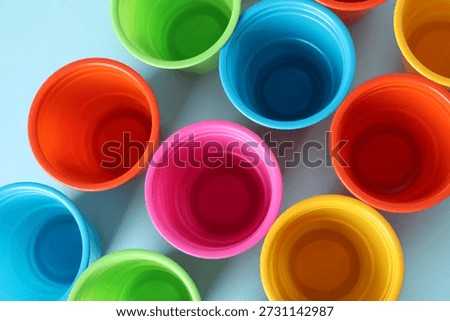 Plastic packaging. Set of bright disposable cups on light blue background, flat lay