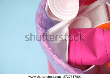 Plastic packaging in trash bin on light blue background, closeup. Space for text
