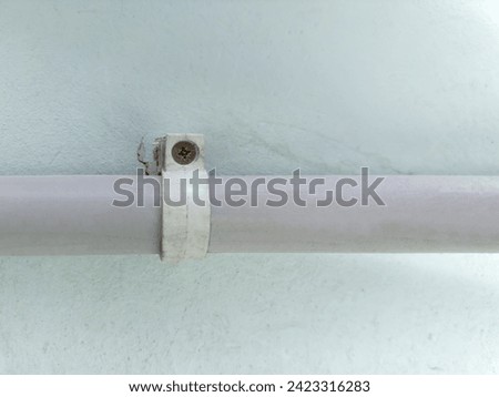 Plastic pipe, as duct for pulling of communication cables fixed to a concrete wall with plastic pipe clamp and screw indoor, close-up in selective focus
