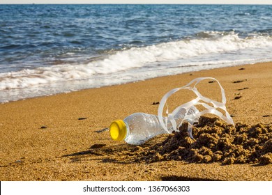 Plastic Pollution. A Plastic Bottle And A Six Pack Plastic Rings On The Beach Shore