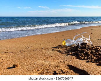 Plastic Pollution. A Plastic Bottle And A Six Pack Plastic Rings On The Beach Shore