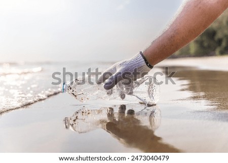 Plastic pollution and environmental problem concept. Close up of male volunteer hand with collecting plastic bottle on the beach. Greening the planet. Recycle reduce and reuse concept.