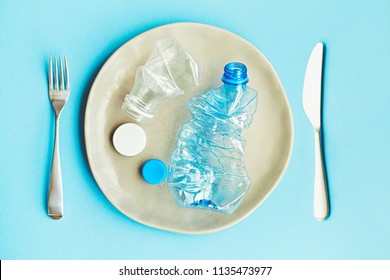 Plastic Pollution Of Food Concept, Handmade Plate With Plastic Bottles And Caps On Blue Background
