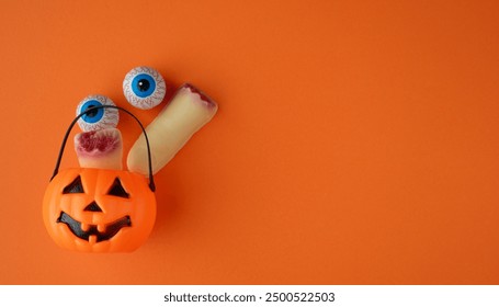 Plastic pumpkin with chocolate eyes and fingers on an orange background. Halloween invitations, banners, posters, space to write - Powered by Shutterstock