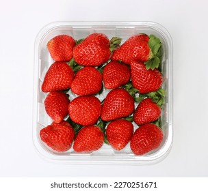 Plastic punnet full of lush strawberries against plain white background