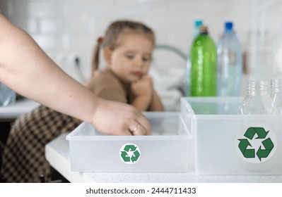 Plastic recycling. Mom teaches her cute daughter to sort plastic in the kitchen. The daughter helps her mother wash plastic bottles and put them in boxes for recycling. Eco-friendly concept. - Powered by Shutterstock