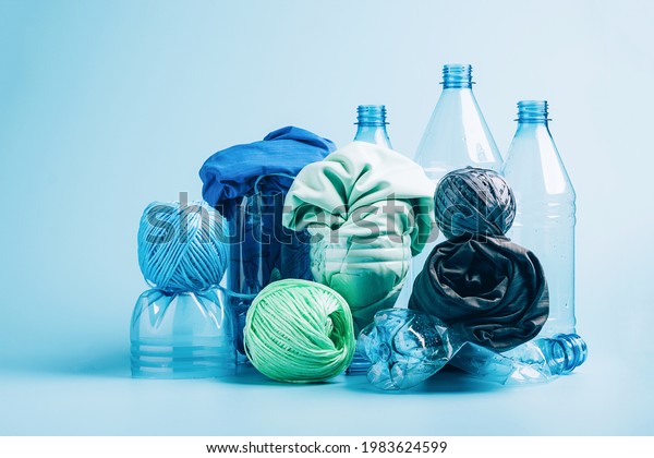 Plastic recycling and reuse concept. Empty\
plastic bottle and various fabrics made of recycled polyester fiber\
synthetic fabric on a blue background. Environmental protection\
waste recycling.