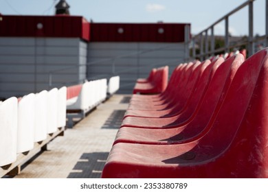 Plastic seats on the grandstand for spectators in the mud. Dirty old red seats in an open-air sports stadium