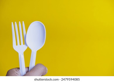 Plastic spoon and fork are held by hand on a yellow background. Close-up plastic cutlery texture. Concept of tools for food, and delivery equipment. Plastic fork and spoon in hand with copy space.