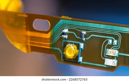 Plastic strip with flexible printed circuit and electronic surface mounted components. Closeup of bent ribbon cable with green and yellow lines of flat PCB dismantled from headphones. E-waste recycle.