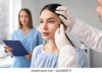 Plastic surgeon applying marks on patient's face in clinic - Powered by Shutterstock