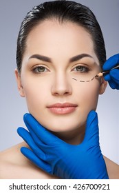 Plastic Surgeon Drawing Dashed Line Under Eye Of Girl. Beautiful Girl. Hands In Blue Glove Holding Pencil And Face. Plastic Surgery, Beauty Portrait