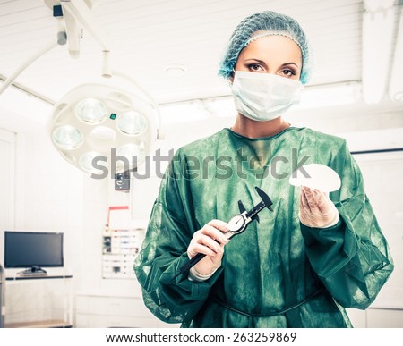 Plastic surgeon woman with silicon breast implant and calliper in surgery room