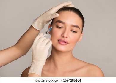 Plastic Surgery And Beauty Injection Concept. Young Woman Receiving Botox For Wrinkles, Isolated Over Studio Wall