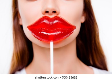 Plastic surgery concept. Cropped close up photo of young woman holding big red lips shaped candy near the mouth on white background