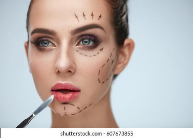 Plastic Surgery Operation. Closeup Beautiful Young Woman With Fashionable Makeup Holding Scalpel. Portrait Healthy Female Model With Black Lines On Face. Facial Beauty Treatment. High Resolution