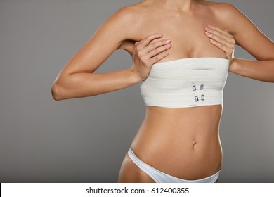 Plastic Surgery. Young Woman With Beautiful Slim Sexy Body Posing On Grey Background. Closeup Of Fit Female Patient Figure With Breast Covered In Medical Bandage. Cosmetology. High Resolution