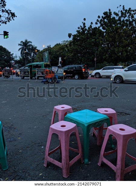 Plastic tables and chairs for people to eat\
outside. In the background we have trees and vehicles. In the image\
we have the colors White, Green, Grey, Pink, Blue. Bali, Indonesia.\
02.11.2022
