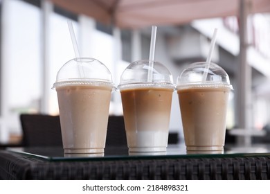 Plastic Takeaway Cups Of Delicious Iced Coffee On Table In Outdoor Cafe